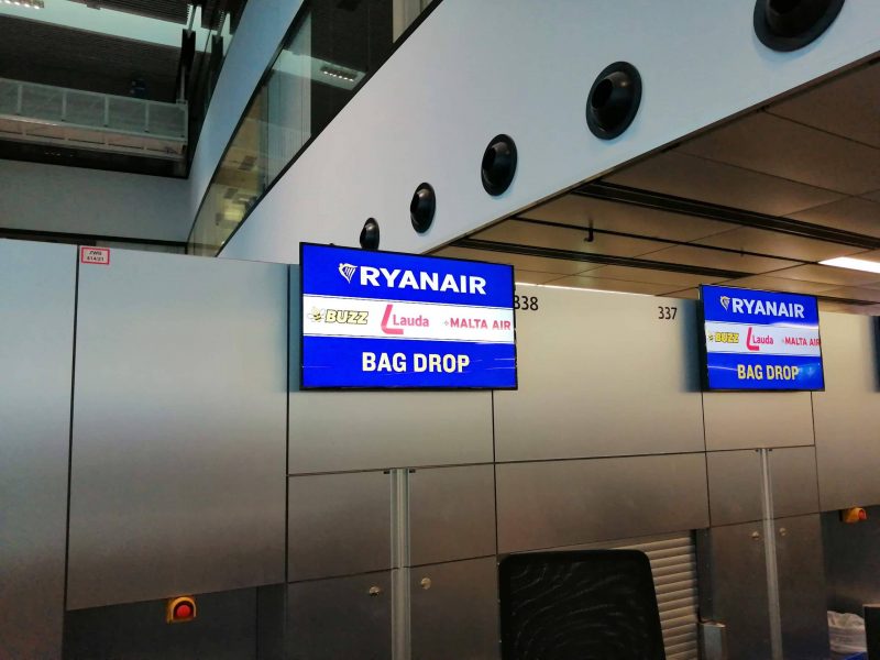 Screen über einem Gepäckabgabeschalter mit den Logos von Ryanair, Buzz, Lauda und Malta Air (Foto: Jan Gruber)